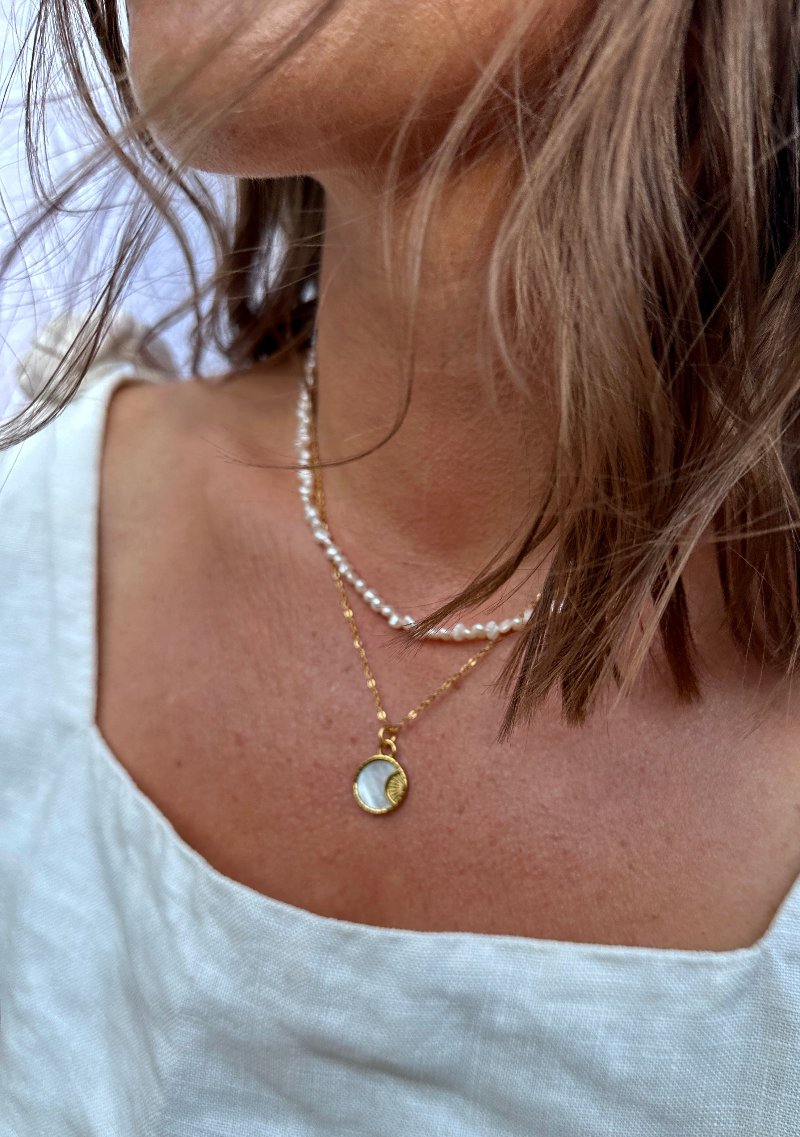 Women wearing gold pendant necklace with a mother of pearl choker necklace